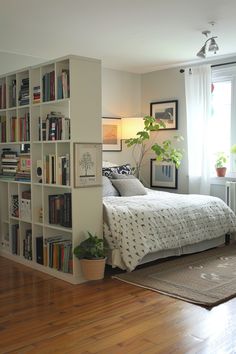 a bedroom with a bed, bookshelf and plant in the corner next to it