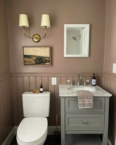 a white toilet sitting next to a bathroom sink under a vanity with a mirror above it