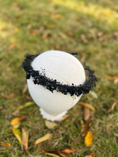 a white ball sitting on top of a lush green field covered in black dirt next to leaves