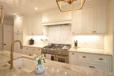 a white kitchen with marble counter tops and gold faucet lighting over the sink