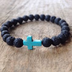 a bracelet with a blue cross on it and black lava beads is sitting on a wooden surface