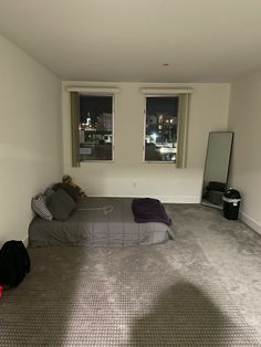 an empty bedroom with two windows and a bed in the corner next to a suitcase