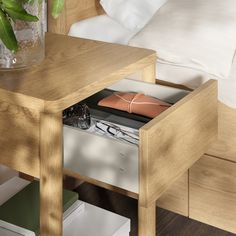 an open drawer in a wooden table next to a bed