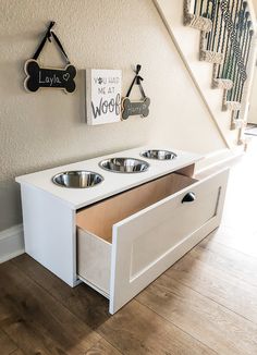 a white dog house with two bowls in the bottom drawer and a sign on the wall above it