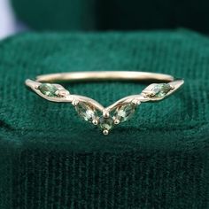 a gold ring with three green stones on it's side, sitting on top of a green cloth