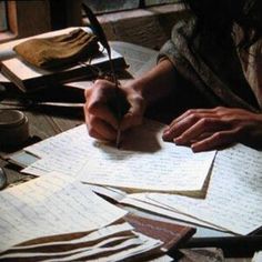 a person sitting at a table with papers and scissors in their hands, writing on paper