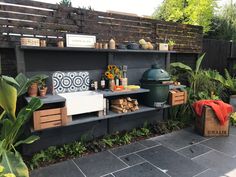 an outdoor kitchen with potted plants and other items on the counter top, next to a grill