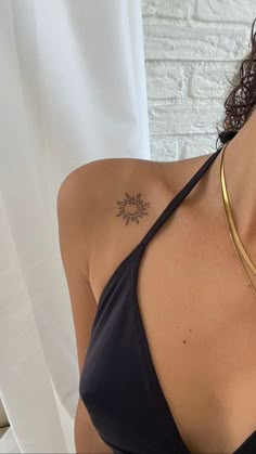 a woman with a tattoo on her chest wearing a halter top and gold necklace