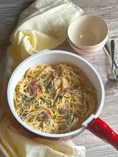 a bowl of pasta with spinach and tomatoes on a wooden table next to a fork