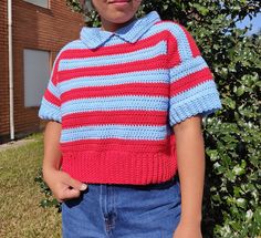 a young boy wearing a red, white and blue sweater standing in front of a bush