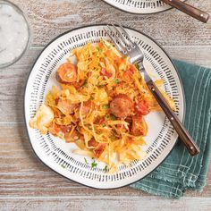 two white plates with pasta and sausage on them next to a glass of water, fork and napkin