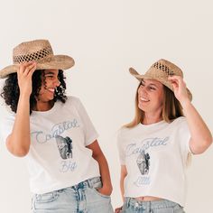 two women wearing matching shirts and cowboy hats, one is holding her hat over the other's head