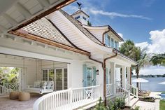 a white house with blue shutters on the front and back porch, overlooking a body of water