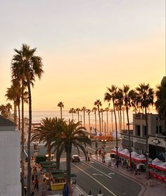 people are walking on the sidewalk next to palm trees and beachfront buildings at sunset