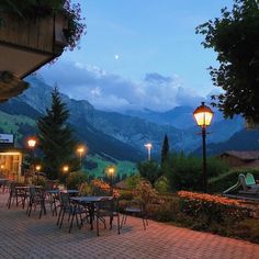 tables and chairs are set up on the patio at dusk with mountains in the background