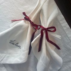 two white napkins with red ribbon tied around them on top of a table cloth