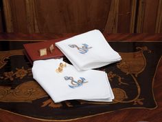 three folded napkins with embroidered anchors on them sitting on a rug in front of a wooden paneled wall