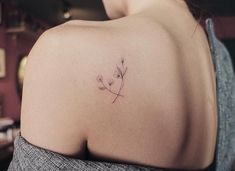 the back of a woman's shoulder with a small flower tattoo on it