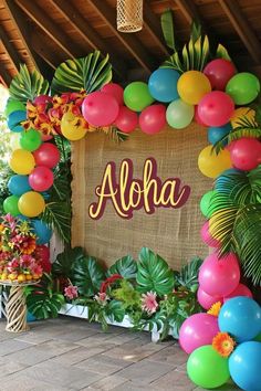 a sign that says aloha surrounded by balloons and palm leaves on the ground