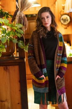 a woman standing in front of a potted plant wearing a sweater and fringe skirt