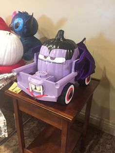 a purple toy truck sitting on top of a wooden table next to two pumpkins