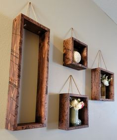 three wooden frames hanging on the wall with flowers in them and one holding a vase