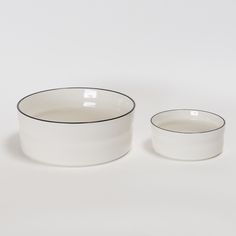 two white bowls with black rims sitting next to each other on a white surface