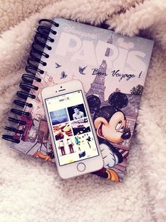 a cell phone sitting next to a book on top of a white fluffy blanket with an image of mickey mouse