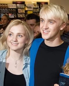 two people standing next to each other holding books