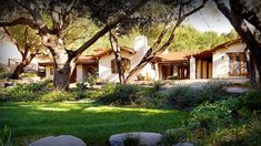 the house is surrounded by many trees and grass, with rocks in front of it