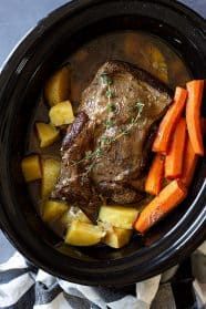 a pot roast with carrots, potatoes and meat in it on a table cloth