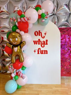 a balloon arch that says oh what fun with balloons surrounding it and a teddy bear holding a candy cane