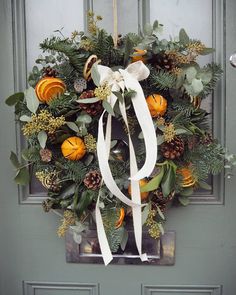 a wreath with white ribbon hanging on the front door, decorated with oranges and greenery