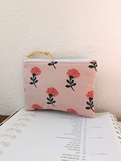 a pink flowered pouch sitting on top of a book next to a white wall