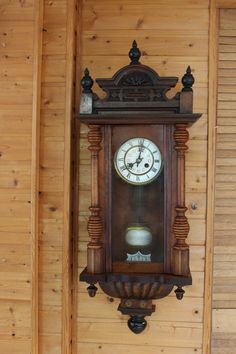 an old wooden clock hanging on the side of a wood paneled wall in a room