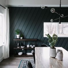 a dining room with green walls and wooden table surrounded by chairs, potted plants and other decorations