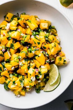 a white bowl filled with pineapple salsa next to lime wedges