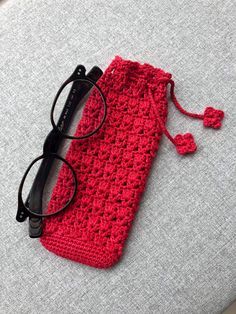 a red crocheted pouch with eyeglasses on the side and a pair of black glasses laying next to it