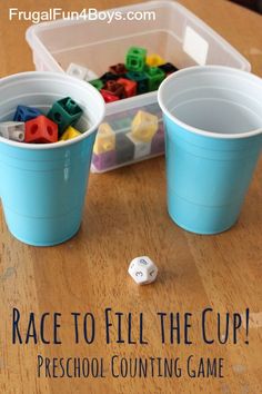 two plastic cups filled with legos sitting on top of a wooden table next to a dice