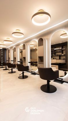 the interior of a modern salon with white walls and flooring, black chairs and round lights