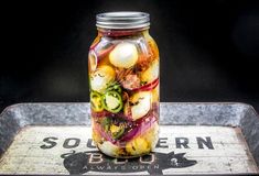 a glass jar filled with pickled vegetables on top of a metal tray next to a sign