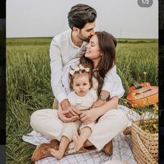 a man, woman and child sitting on a blanket in the middle of a field