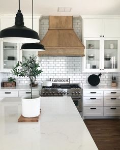 a kitchen with white cabinets and black pendant lights over the stove top, along with a potted plant