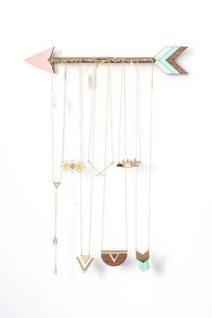 several necklaces hanging on a wall with an arrow and other items attached to it