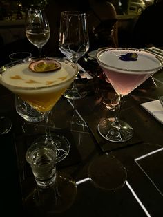 three different types of cocktails on a table with wine glasses in the foreground