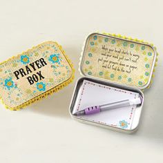 an open tin box with a notepad and pen in it sitting on a table