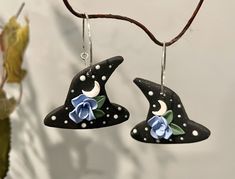 two black witches hats with blue flowers on them hanging from a tree branch in front of a white wall