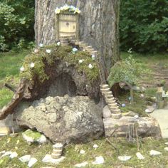 a tree stump with a house built into it in the middle of some grass and rocks