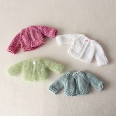 three knitted sweaters are shown on a white surface, one is green and the other is pink