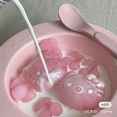 a pink bowl filled with lots of water and gummy bears next to a spoon